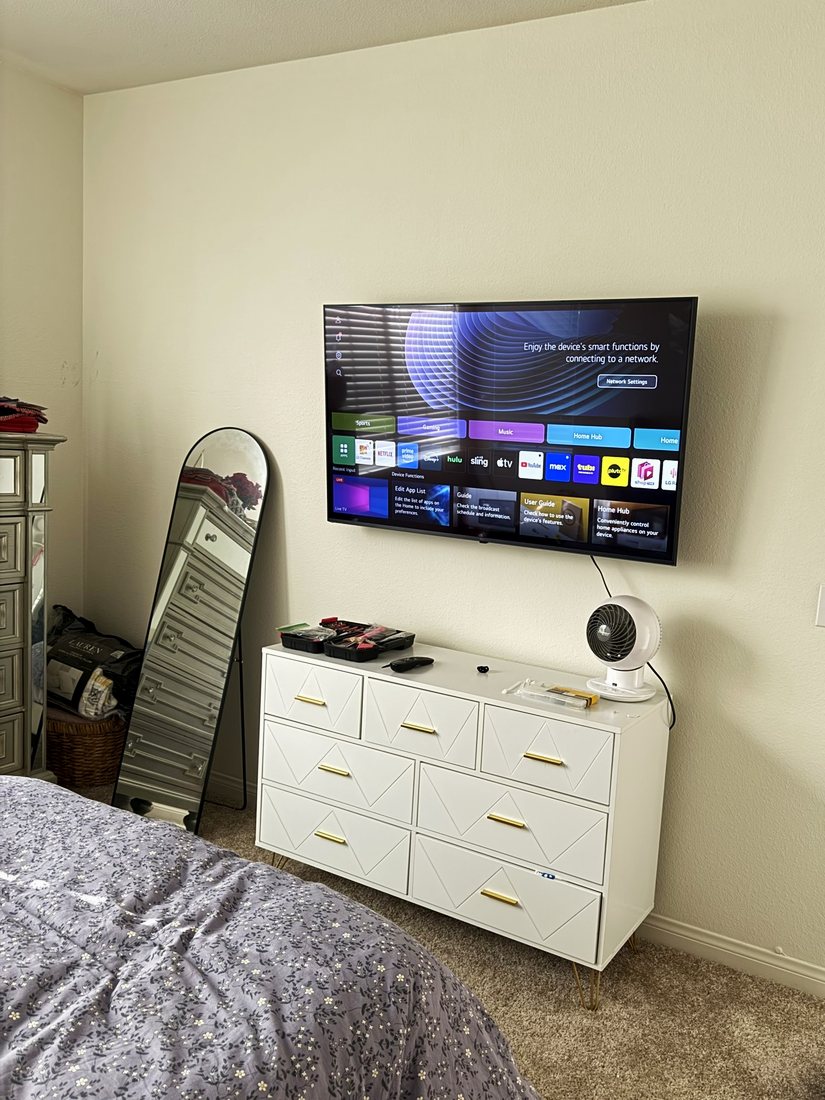 A TV mounted on a bedroom wall above a white dresser with gold handles