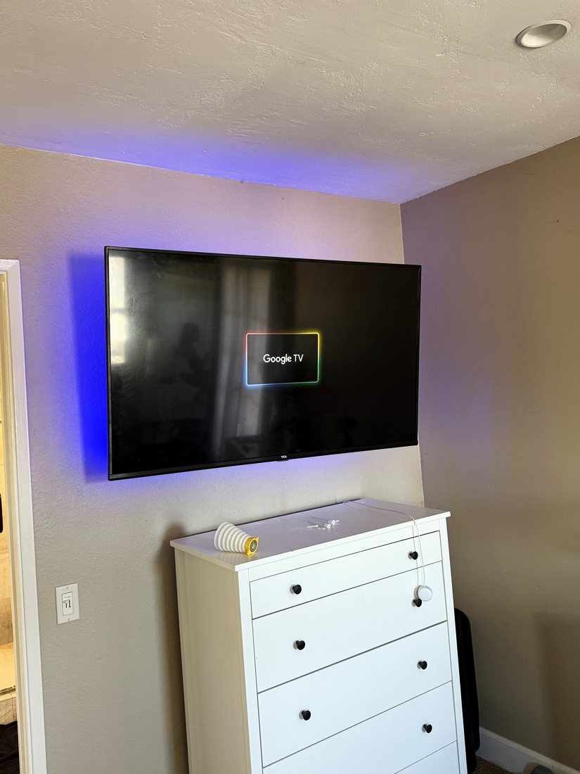 A wall-mounted TV with a blue LED backlight above a white chest of drawers