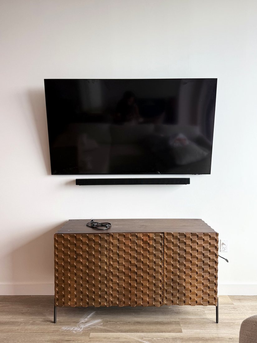 A TV and a slim soundbar mounted on a white wall above a carved wood console