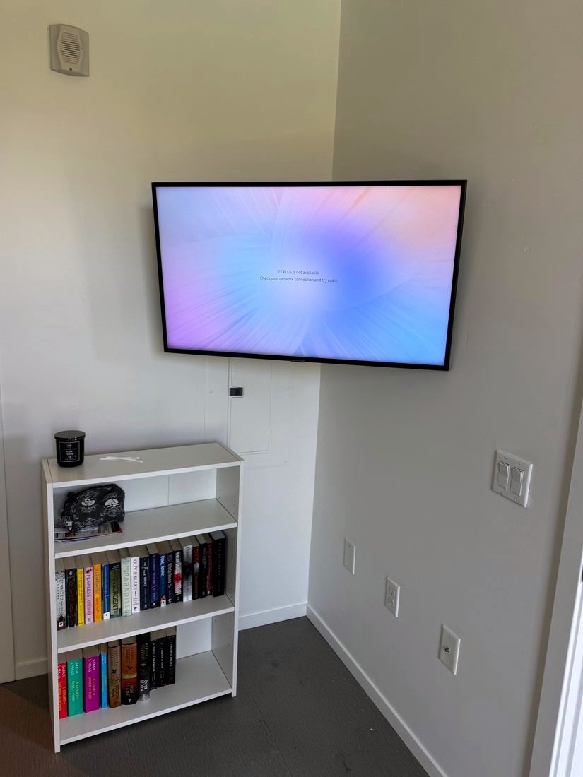 A TV mounted across a room corner above a white bookshelf