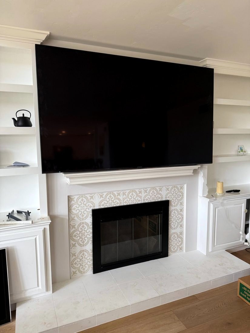A large TV mounted above a white fireplace mantel between built-in shelves