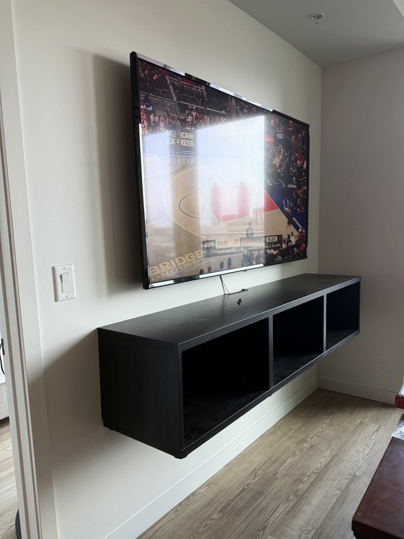 A large TV mounted above a wall-hung black media console in a bright apartment
