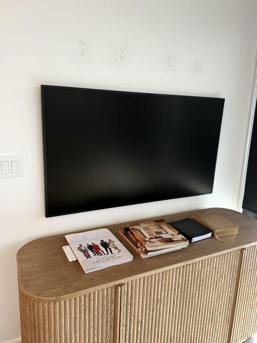 A large TV mounted on a white wall above a rounded fluted wood console