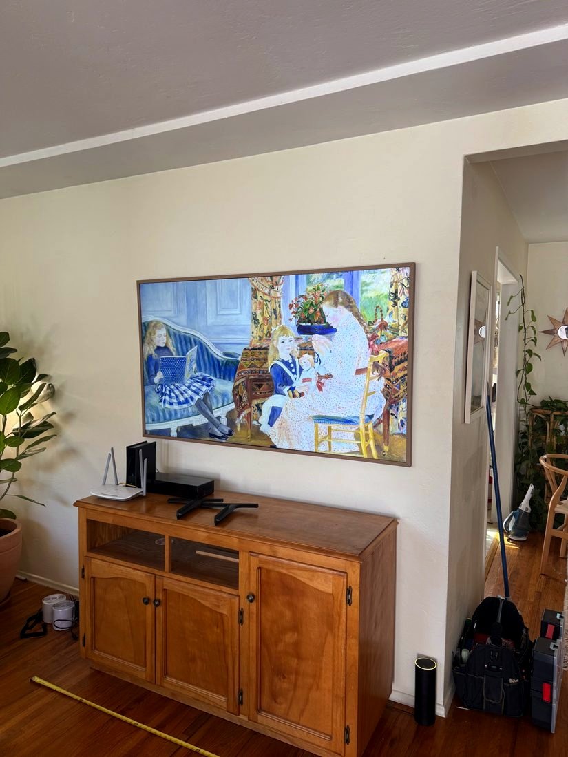 A framed TV showing a painting above a wooden cabinet
