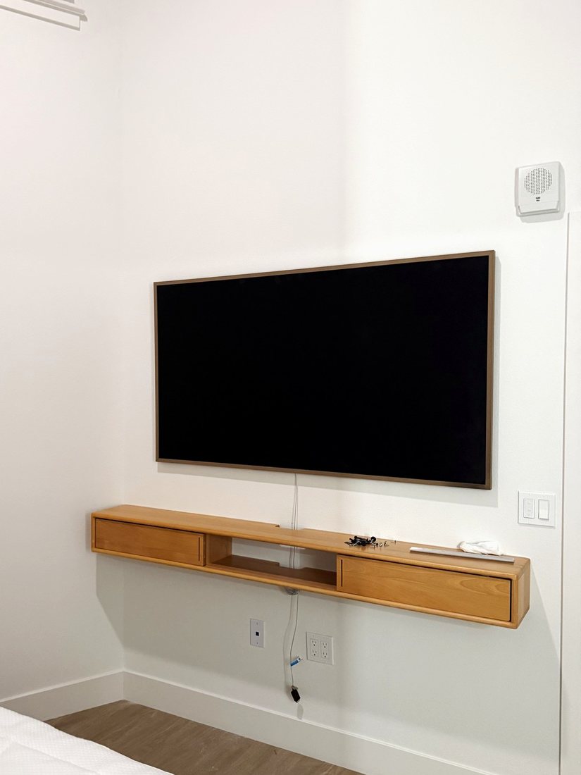 A Frame TV with a wood bezel mounted above a floating wood shelf in a bedroom