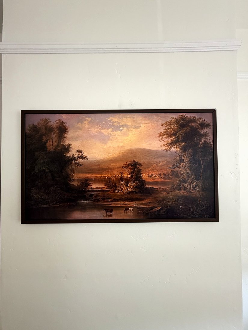 A Frame TV with a dark bezel showing a landscape painting on a white wall