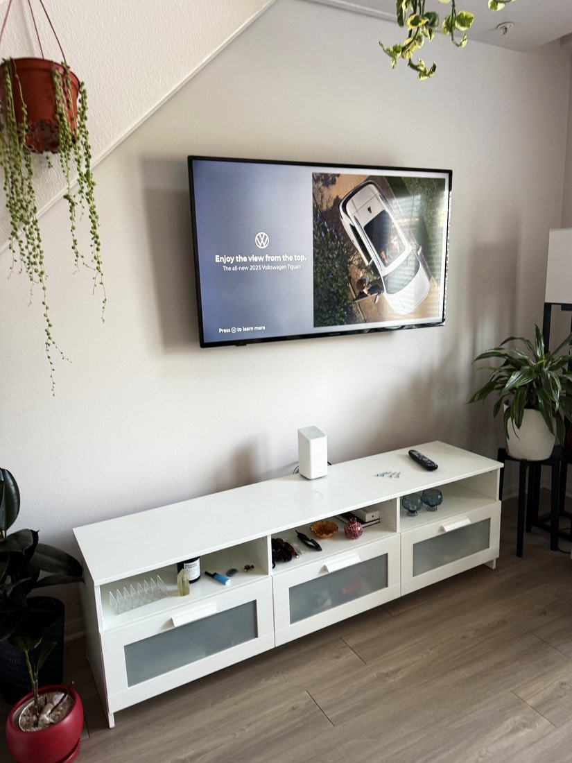 A TV mounted on a white wall above a white console, with hanging plants in a loft