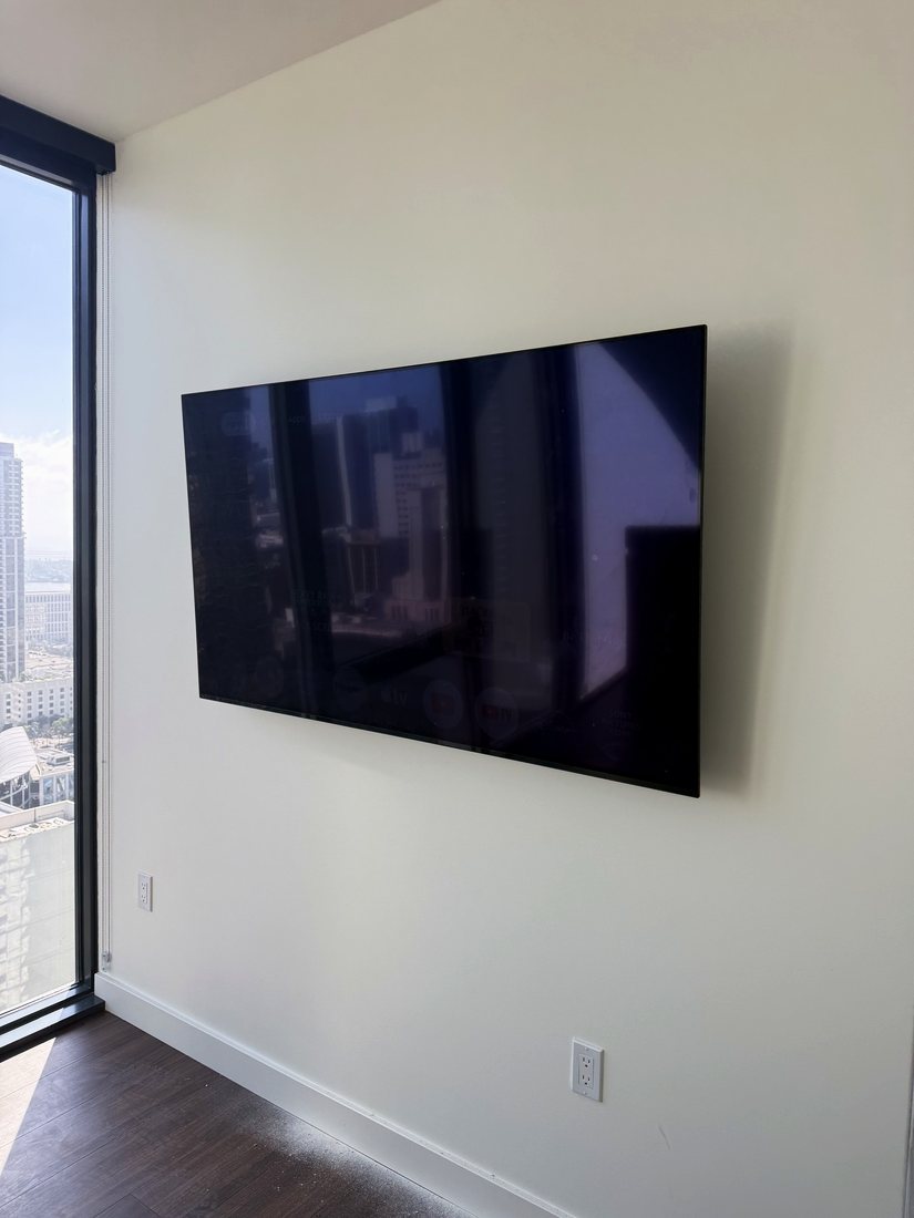 A large TV mounted on a white wall next to a floor-to-ceiling window with a downtown skyline view