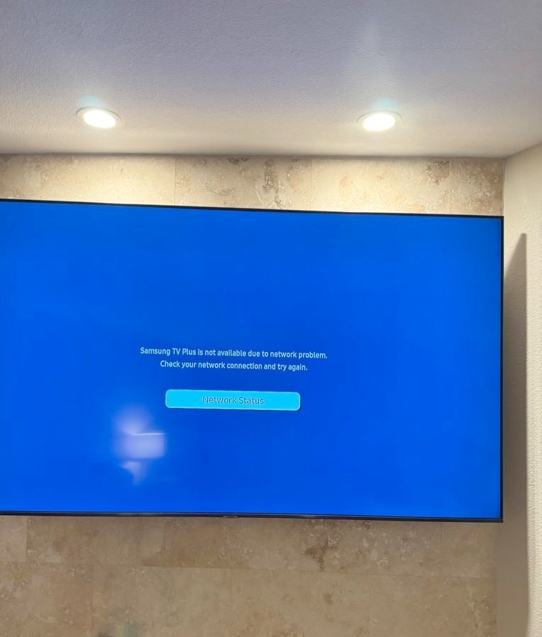 A large TV mounted on a stone tile wall under two ceiling lights