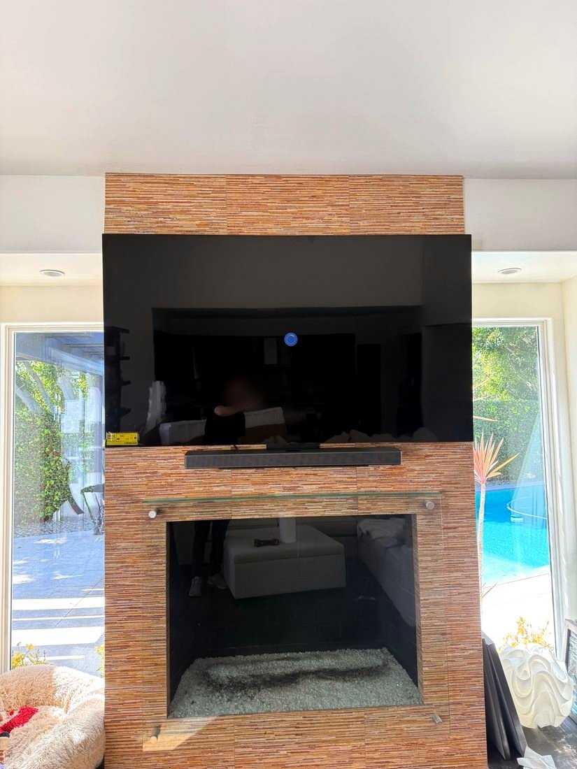 A TV and soundbar mounted on a tiled fireplace column between two windows