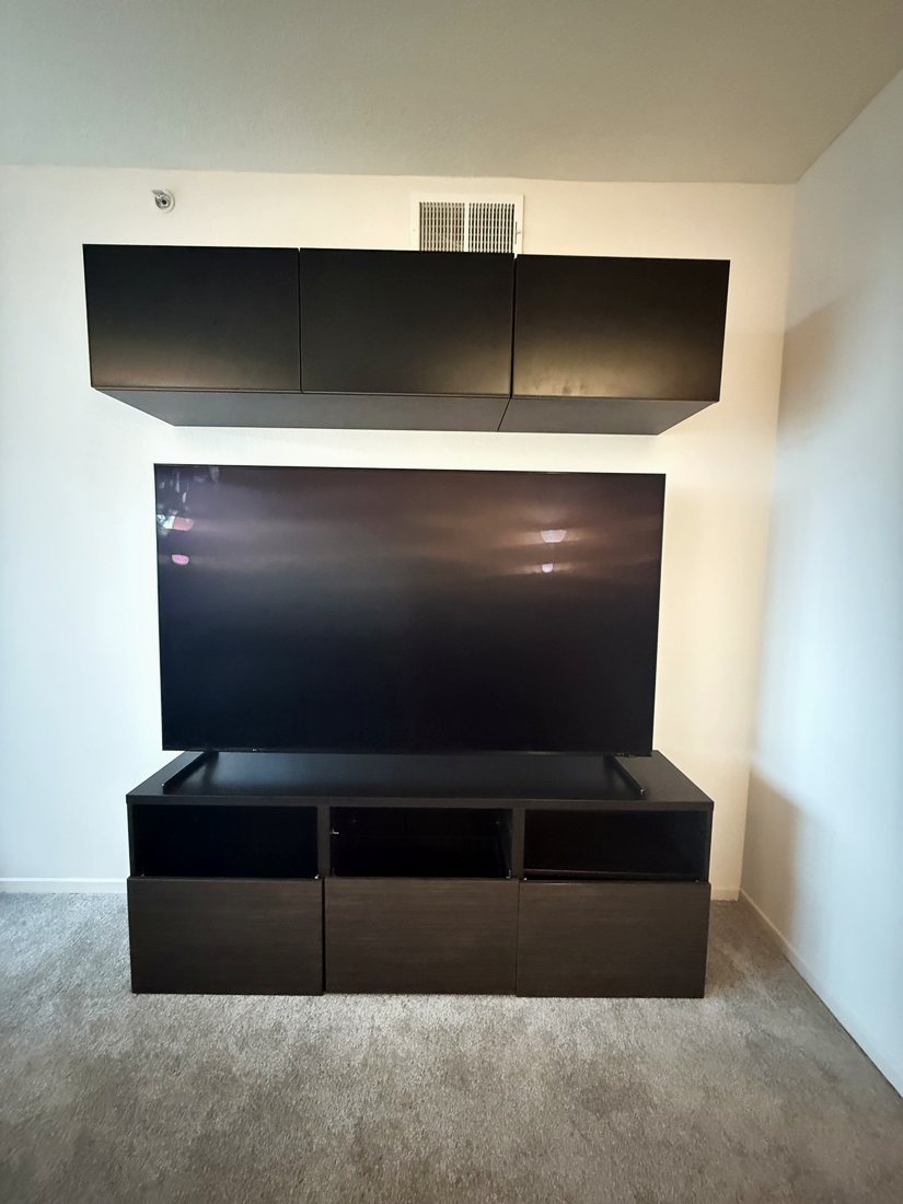 A large TV mounted between black wall cabinets and a matching media console