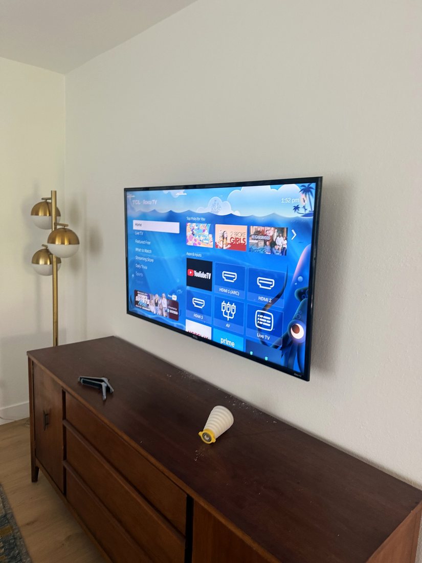 A TV mounted on a white bedroom wall above a walnut dresser