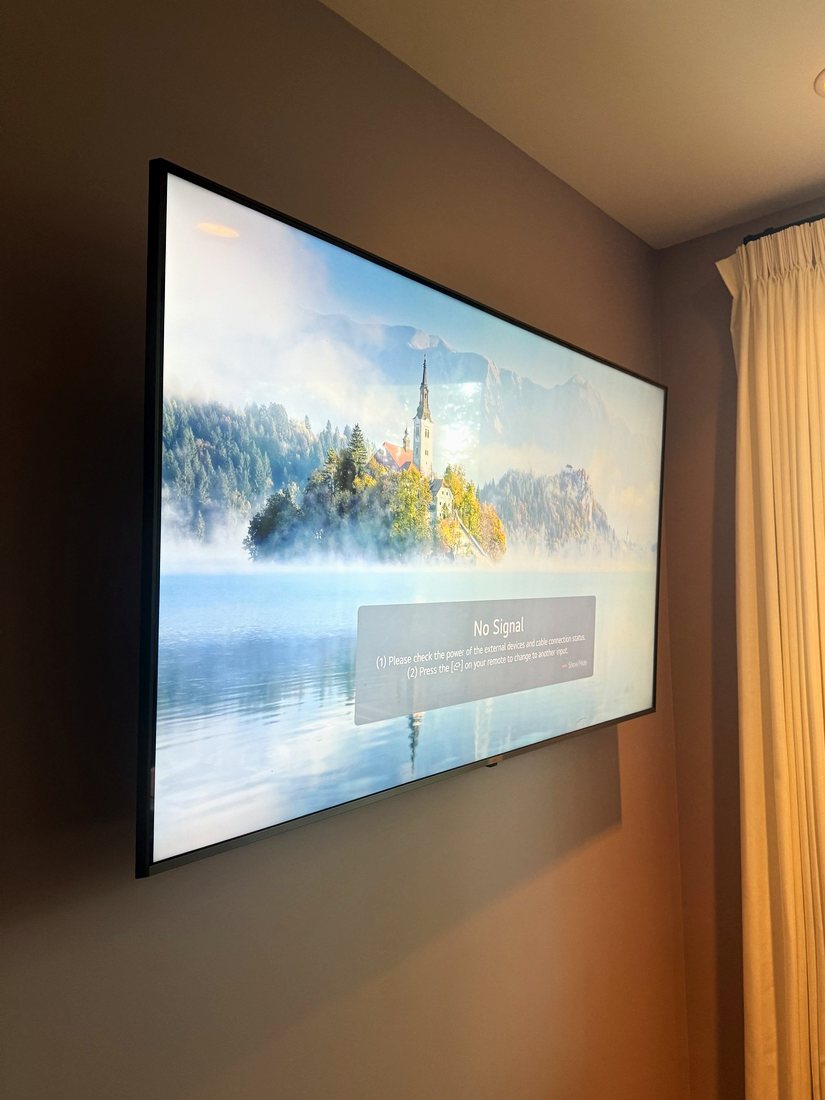 A large TV mounted flush on a taupe wall beside cream curtains