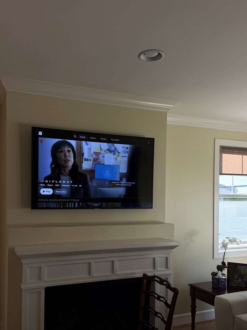A TV mounted above a white fireplace mantel in a living room
