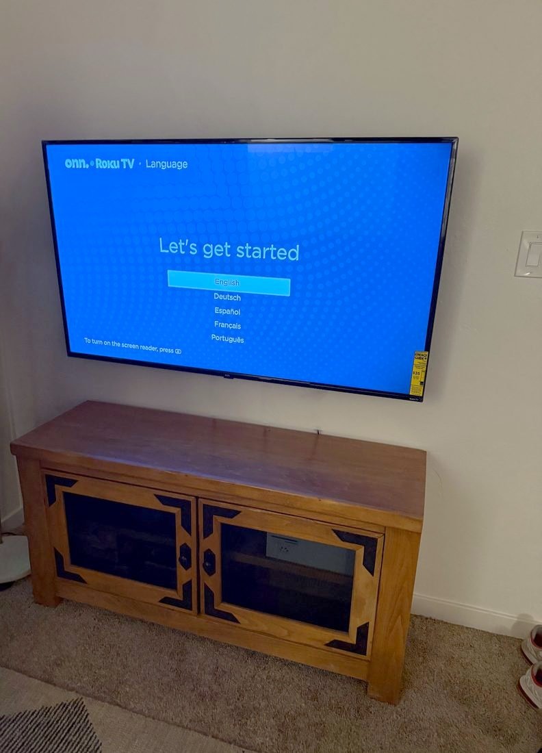 A TV mounted above a wooden media console showing its first setup screen
