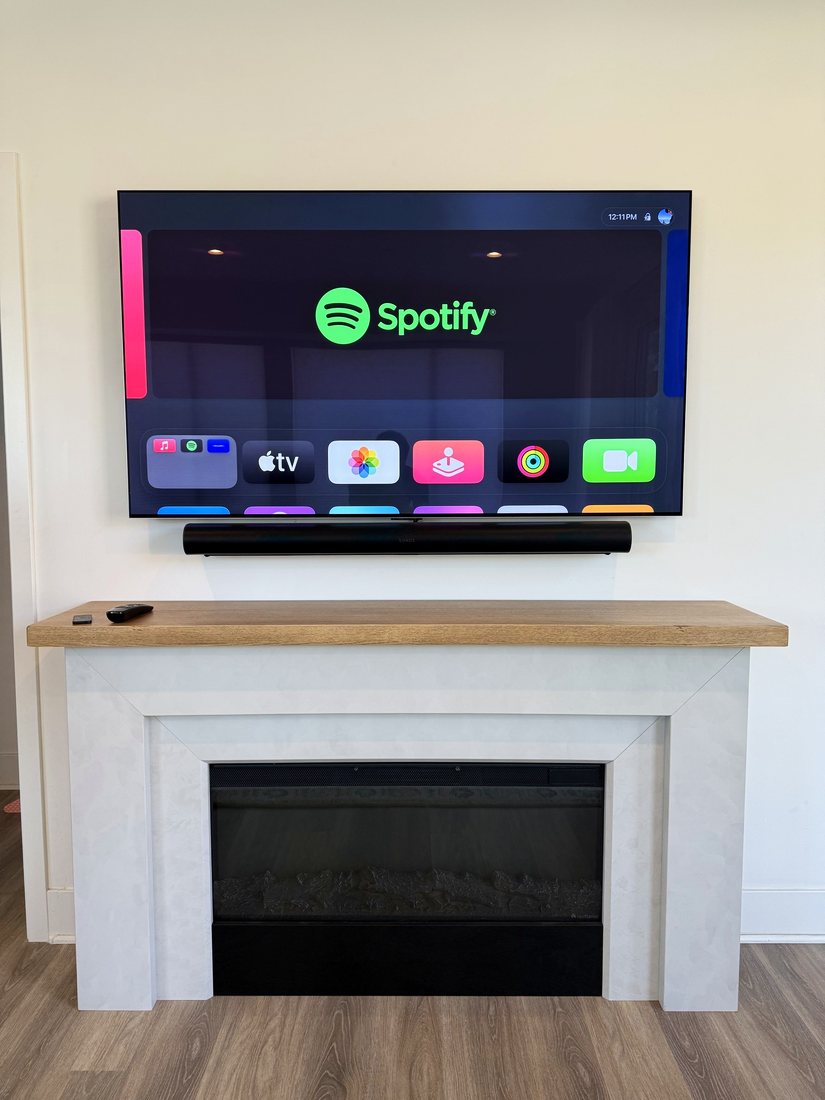 A TV and soundbar mounted above a white fireplace with a wood mantel